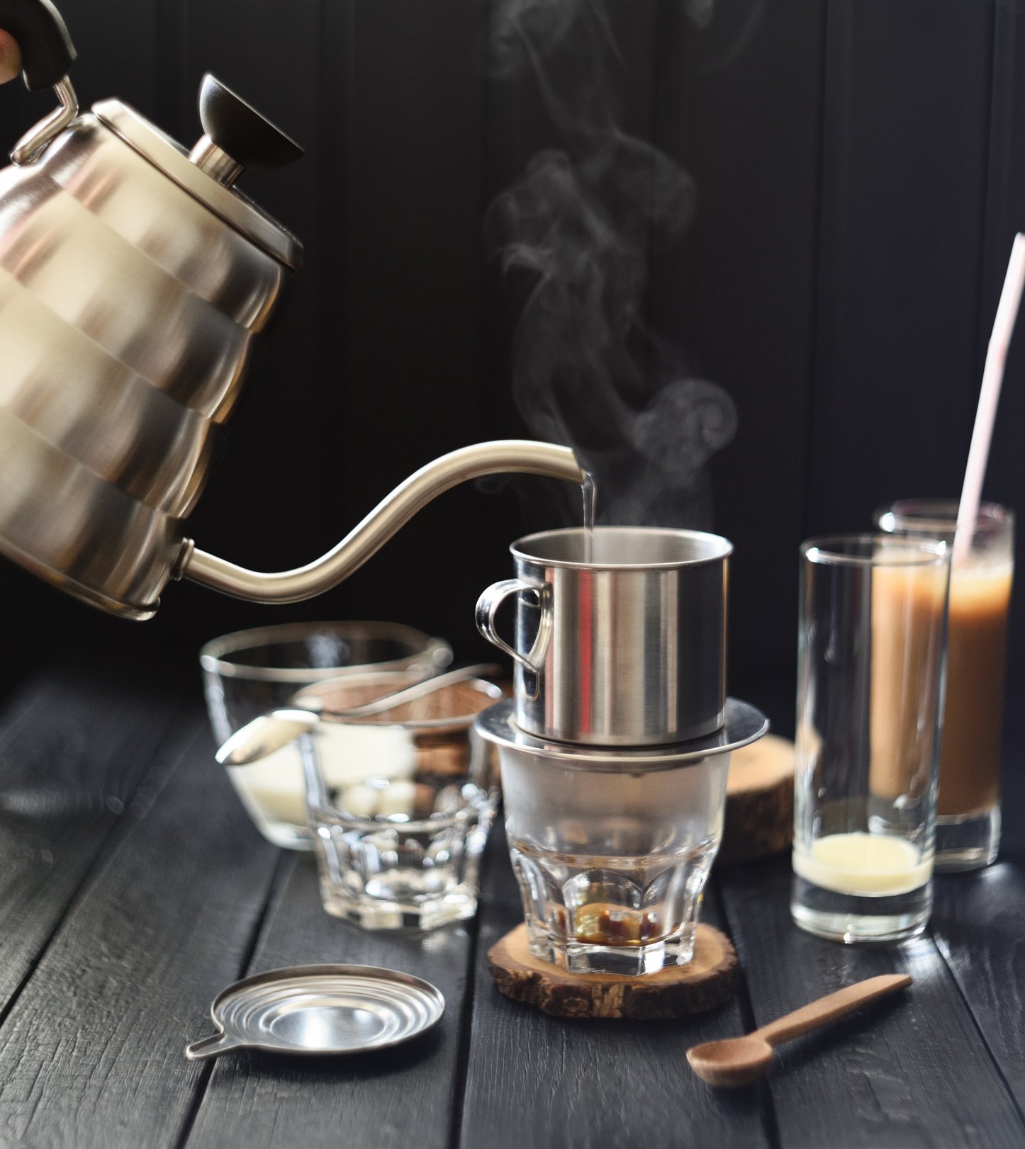 Making Vietnamese drip coffee. Pouring steaming hot water into phin from goose neck kettle on black background